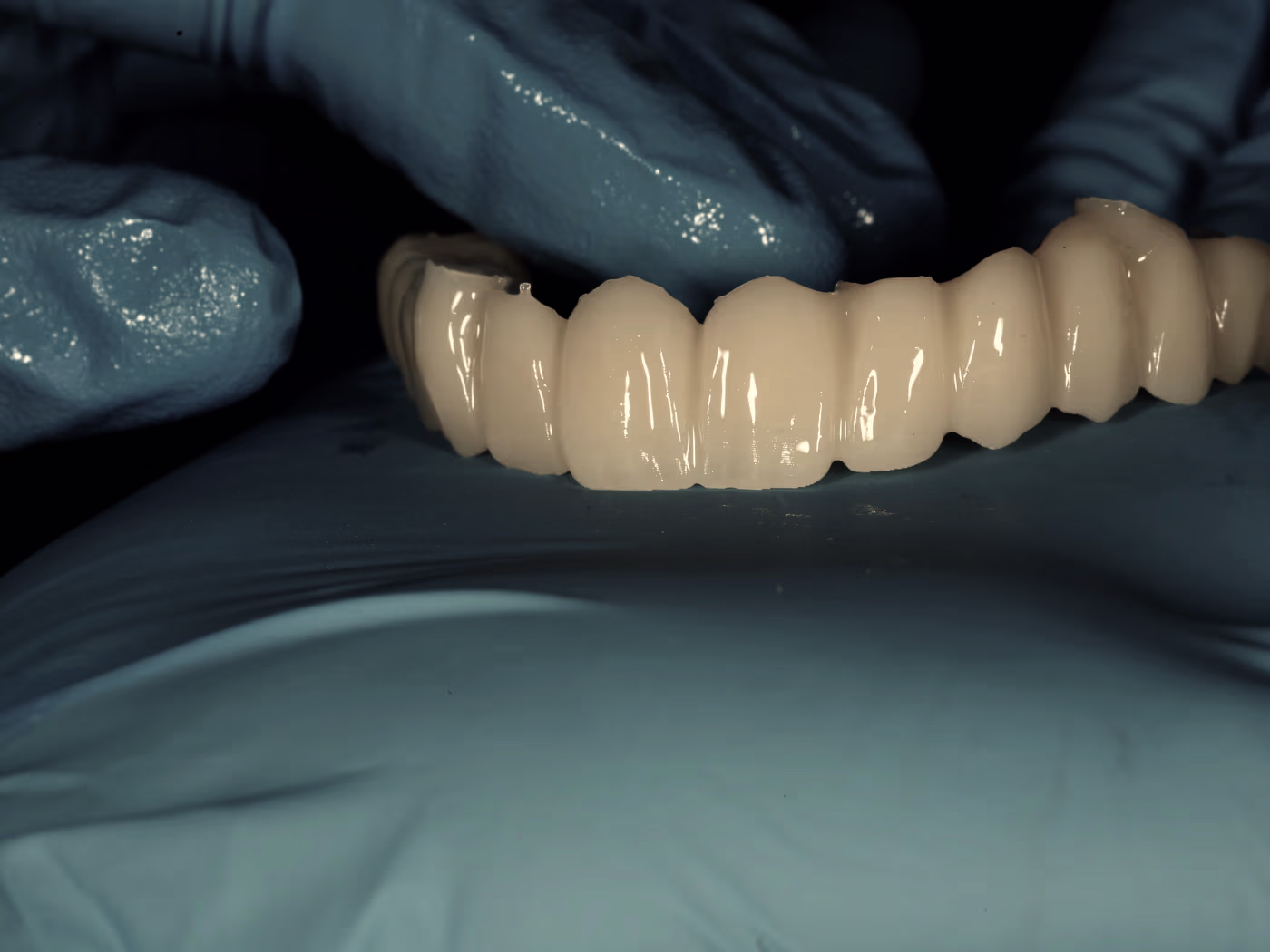 A monolithic full-arch bridge held in gloved hands, out of the mill and before characterisation